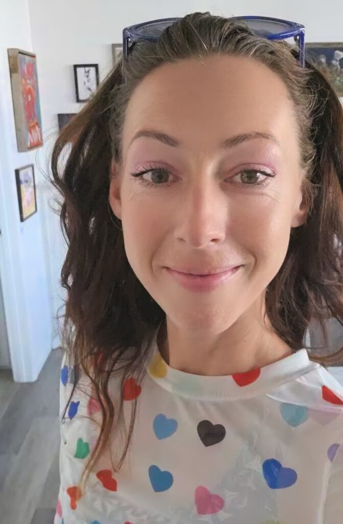 Close-up selfie of Erica, a smiling woman wearing a white shirt with colorful hearts and sunglasses on head